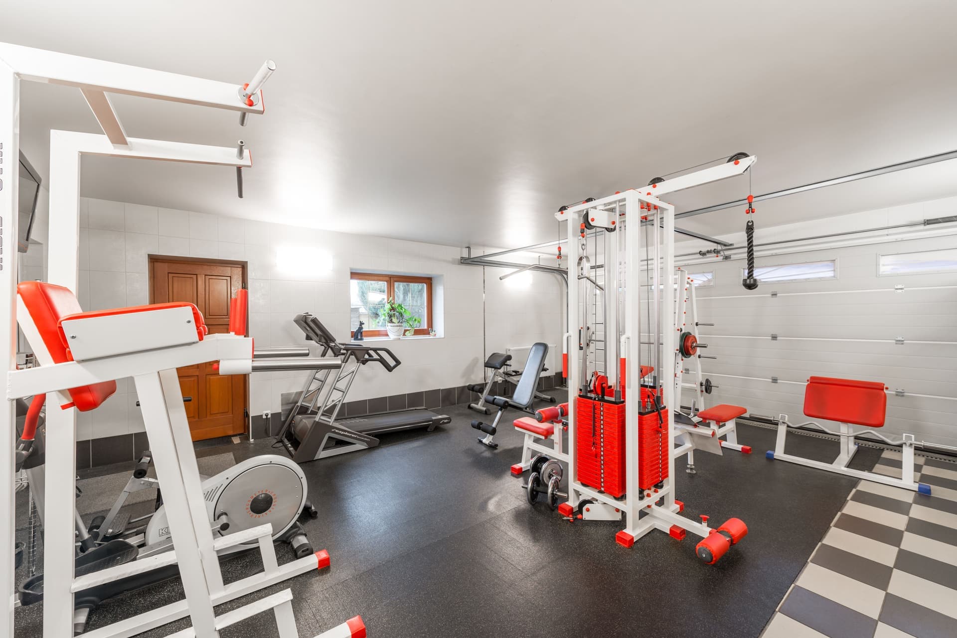 A home gym in a garage with a rack of dumbbells, a barbell and a bench in natural light